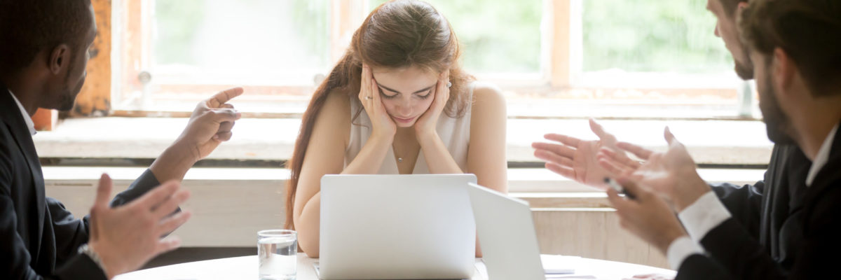 CAI WEBSITE PIC - WOMAN IN UPSETTING BUSINESS MEETING - FRUSTRATED, ANGRY, BULLYING IN THE WORKPLACE - bigstock--221702167 Male colleagues pointing fingers at upset female boss on meeting, tired sad woman leader experiencing gender discrimination at work, businessmen blaming bullying depressed businesswoman for mistake